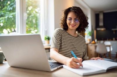 Woman looking at a laptop and writing information down.